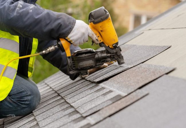 Workman using pneumatic nail gun install tile on roof of new hou